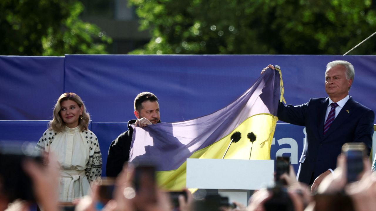 Ukrainian President Volodymyr Zelensky and Lithuanian President Gitanas Nauseda hold a Ukrainian flag from the front line of the war with Russia, next to Olena Zelenska, in Vilnius on July 11, 2023.